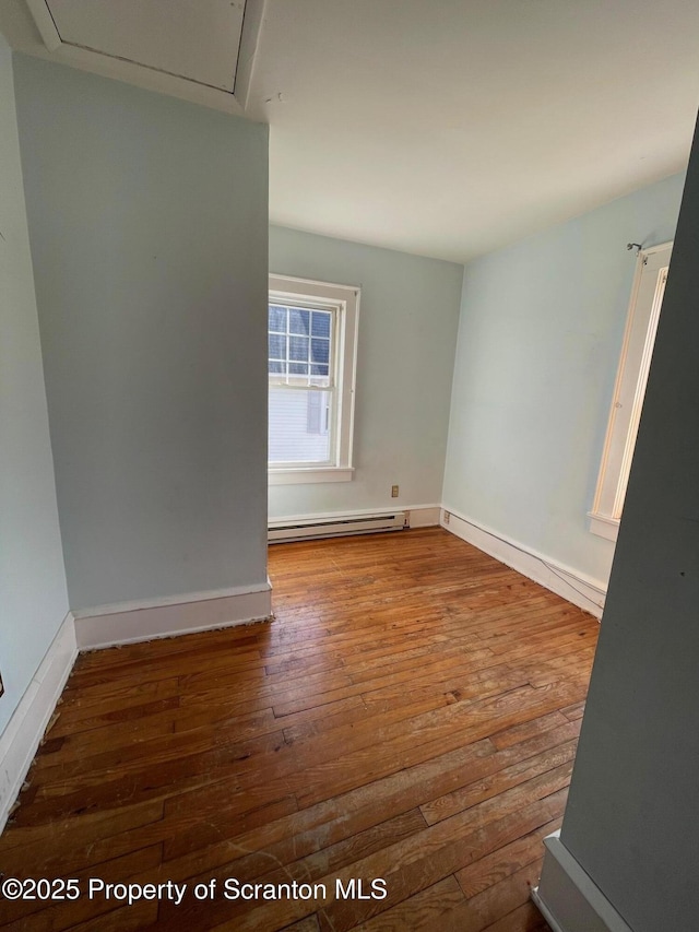 empty room with a baseboard heating unit, wood-type flooring, and baseboards