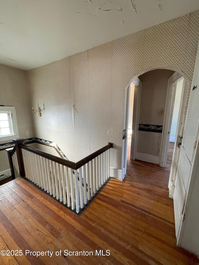 staircase with arched walkways, hardwood / wood-style floors, and wallpapered walls