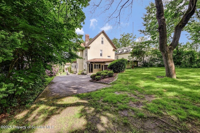 1614 Jefferson Ave, Dunmore, PA 18509 - rear view of house with stucco siding, a chimney, and a lawn