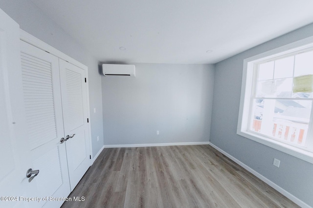 unfurnished bedroom with light hardwood / wood-style floors, an AC wall unit, and a closet