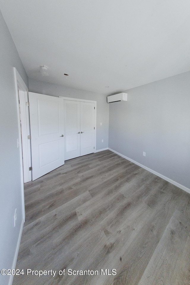 unfurnished bedroom featuring light hardwood / wood-style floors, an AC wall unit, and a closet