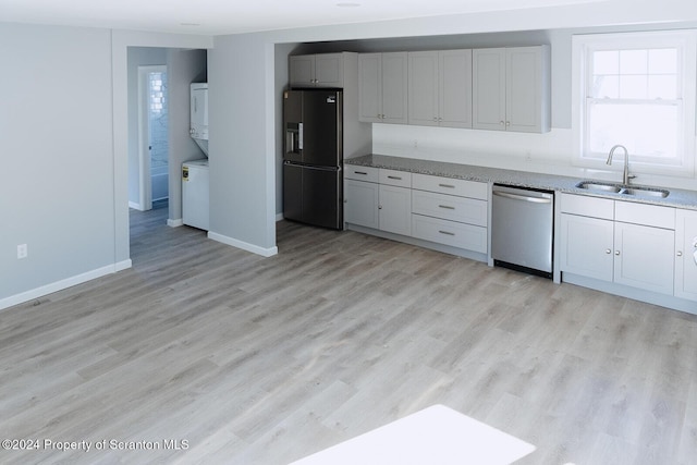 kitchen with light wood-type flooring, light stone counters, stainless steel appliances, sink, and stacked washer / dryer