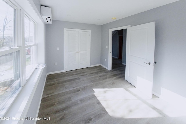 unfurnished bedroom featuring a wall mounted air conditioner, hardwood / wood-style flooring, and a closet