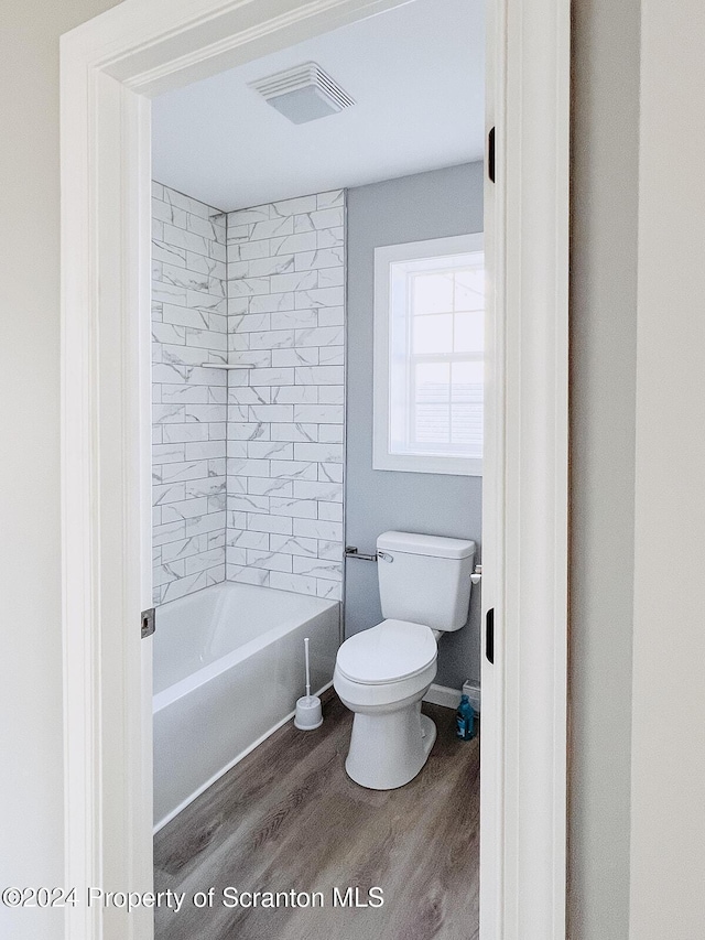 bathroom featuring wood-type flooring, tiled shower / bath combo, and toilet