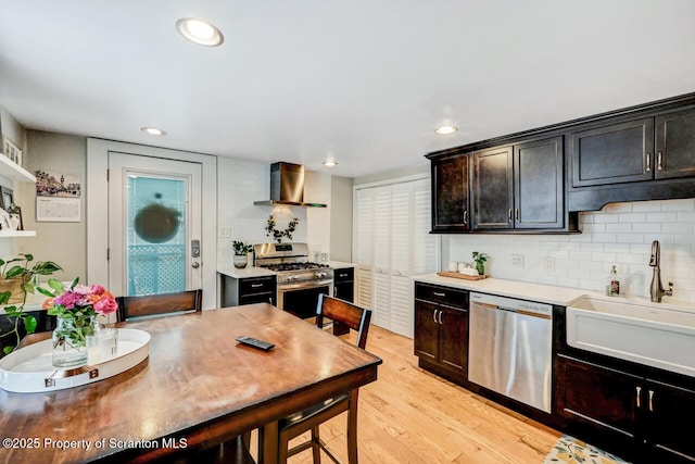 kitchen with tasteful backsplash, sink, light wood-type flooring, stainless steel appliances, and wall chimney exhaust hood