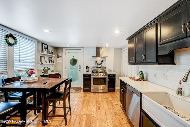 kitchen with light hardwood / wood-style floors, tasteful backsplash, sink, stainless steel appliances, and wall chimney exhaust hood