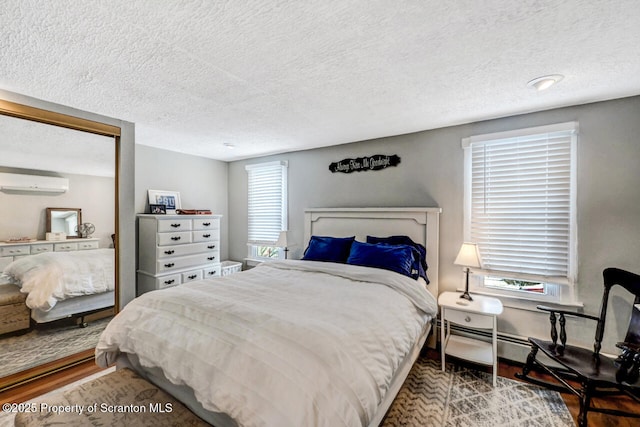 bedroom with an AC wall unit, a textured ceiling, and hardwood / wood-style flooring