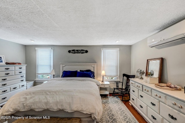 bedroom with a wall mounted AC, dark hardwood / wood-style floors, a textured ceiling, and multiple windows