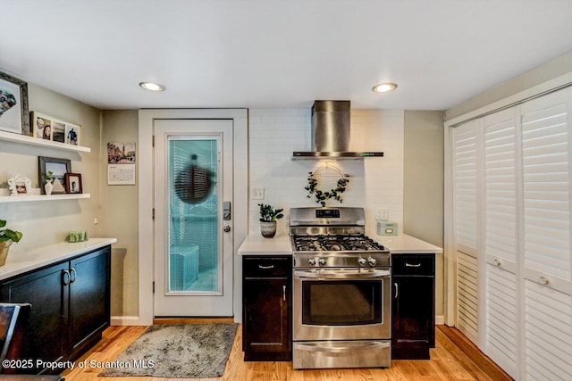 kitchen with wall chimney range hood, light hardwood / wood-style flooring, decorative backsplash, and stainless steel gas stove