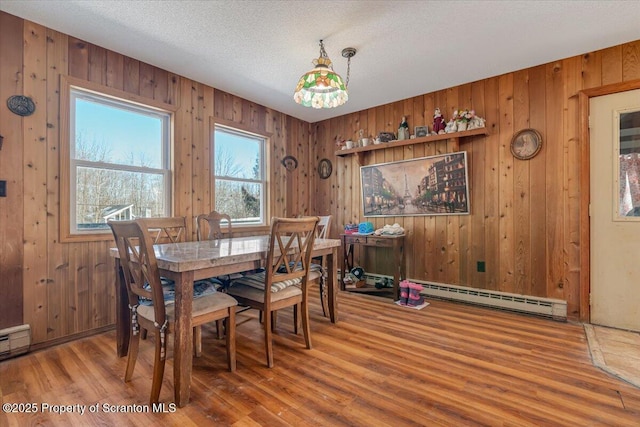 dining area featuring a baseboard radiator, wooden walls, hardwood / wood-style floors, and a textured ceiling