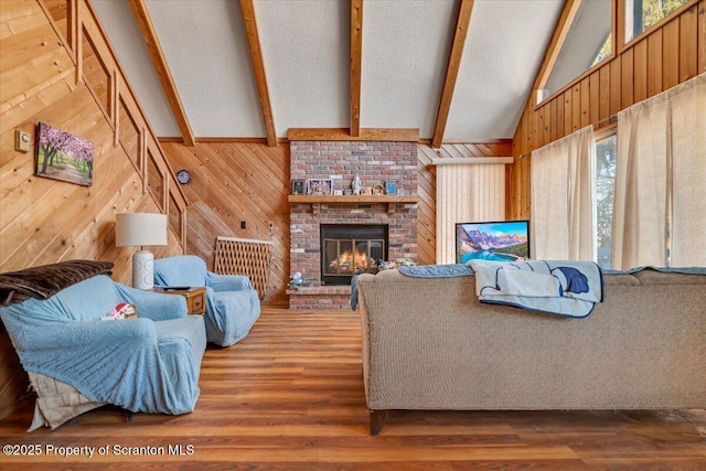 living room with wood walls, vaulted ceiling with beams, a textured ceiling, a brick fireplace, and hardwood / wood-style floors