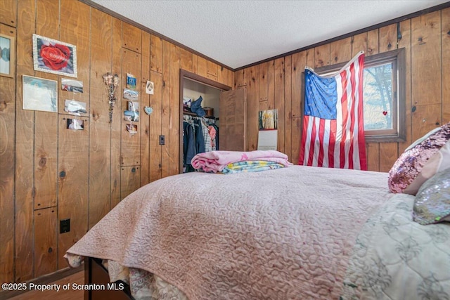 bedroom featuring a walk in closet, a textured ceiling, ornamental molding, wooden walls, and a closet