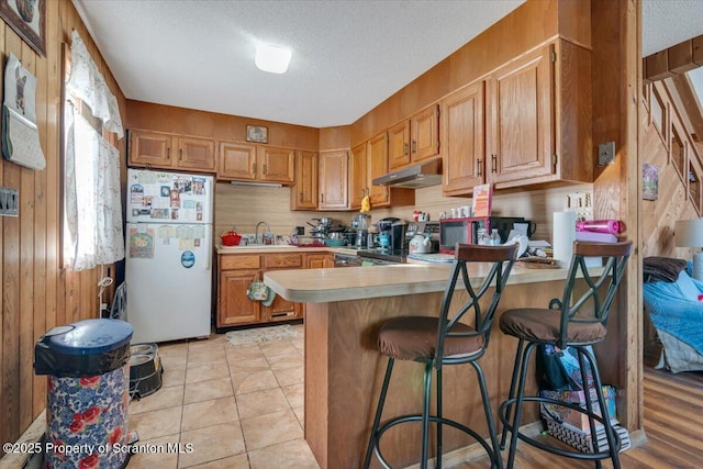 kitchen featuring a breakfast bar, white fridge, a textured ceiling, kitchen peninsula, and wood walls