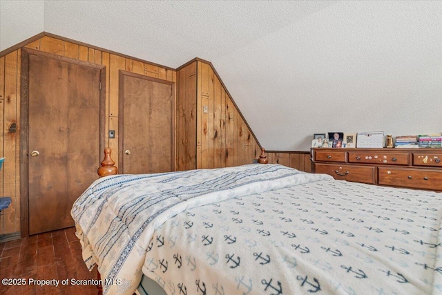 bedroom with lofted ceiling, dark wood-type flooring, a textured ceiling, and wood walls