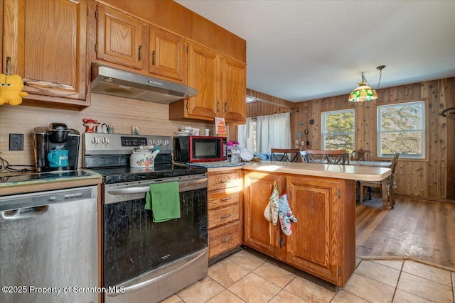 kitchen featuring appliances with stainless steel finishes, pendant lighting, wood walls, light tile patterned floors, and kitchen peninsula