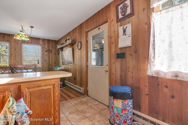 kitchen featuring a baseboard radiator, decorative light fixtures, light tile patterned floors, and wood walls