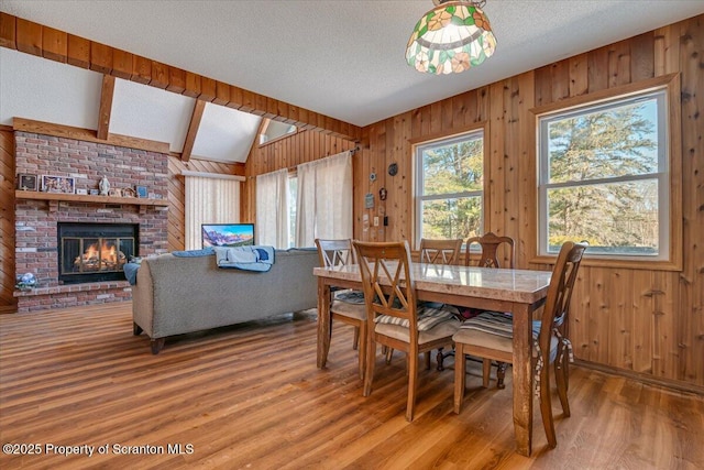 dining area featuring vaulted ceiling with beams, a textured ceiling, wooden walls, hardwood / wood-style flooring, and a fireplace