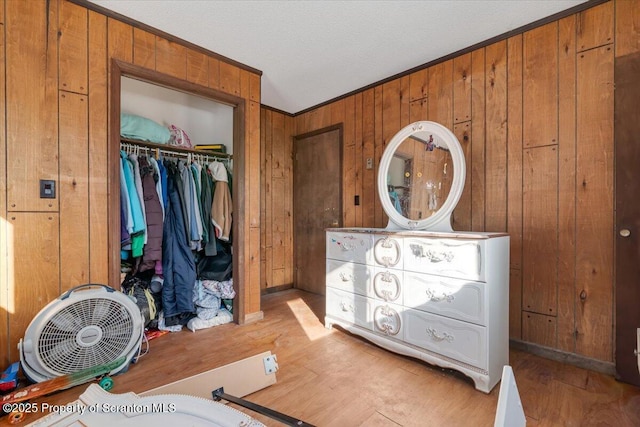 bedroom with light hardwood / wood-style flooring, crown molding, wooden walls, and a closet