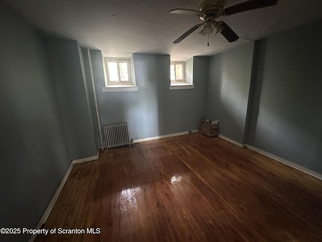 below grade area with radiator, hardwood / wood-style flooring, baseboards, and ceiling fan