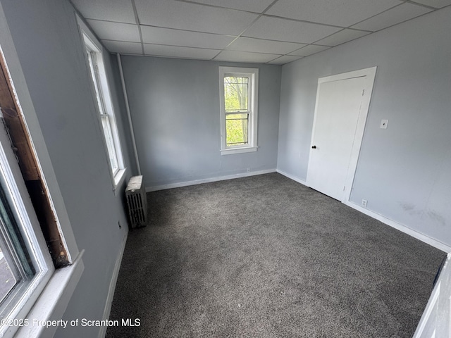 carpeted empty room with radiator heating unit, a drop ceiling, and baseboards