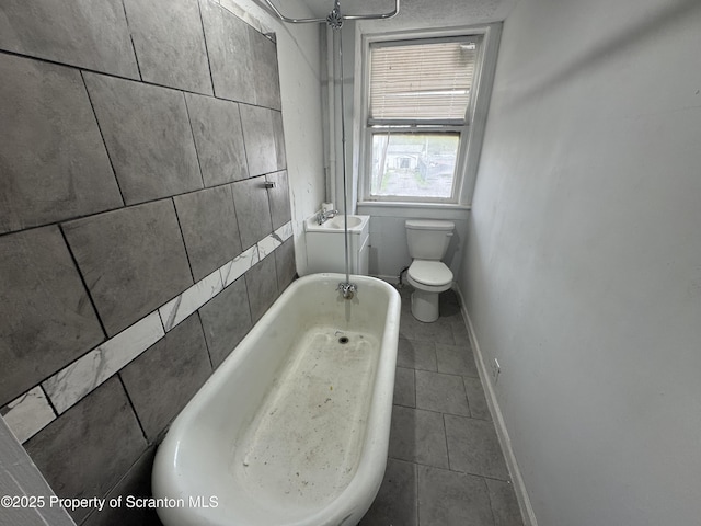 bathroom featuring baseboards, toilet, a bath, and tile patterned floors