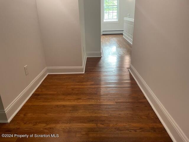 corridor with dark hardwood / wood-style flooring and baseboard heating