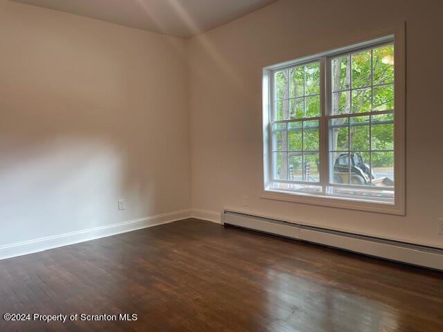 unfurnished room featuring baseboard heating and dark wood-type flooring