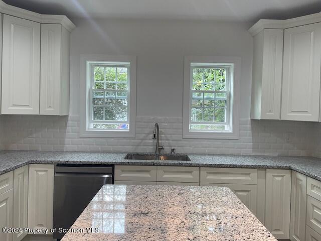 kitchen with light stone countertops, sink, white cabinets, and stainless steel dishwasher