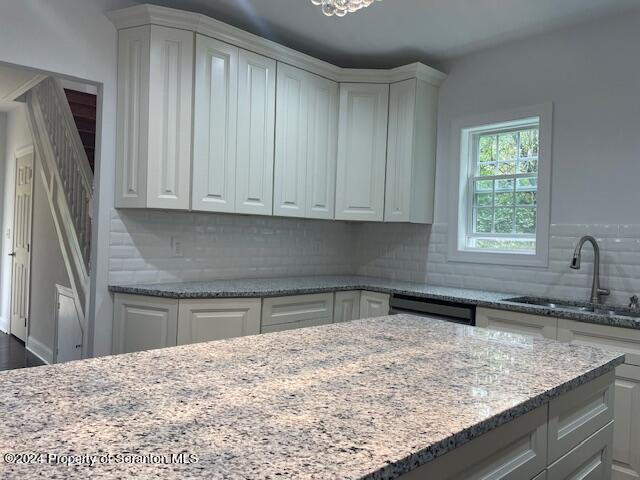 kitchen featuring dishwasher, light stone counters, and sink