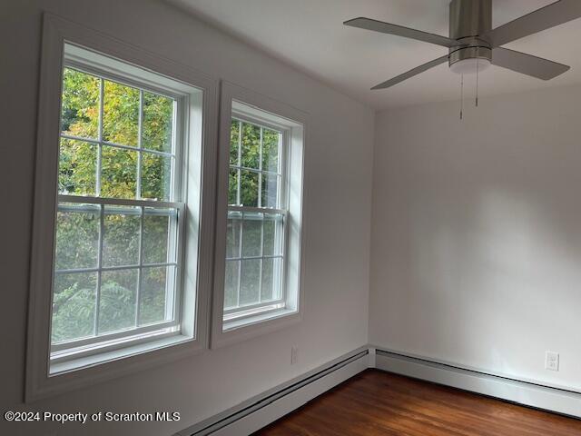 empty room with dark hardwood / wood-style floors, ceiling fan, and a baseboard heating unit