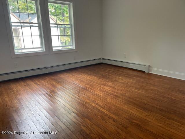 unfurnished room featuring dark hardwood / wood-style flooring and a baseboard heating unit