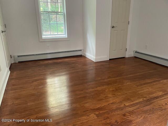 unfurnished room featuring dark hardwood / wood-style flooring and baseboard heating