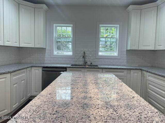 kitchen with dishwasher, white cabinets, light stone counters, and sink