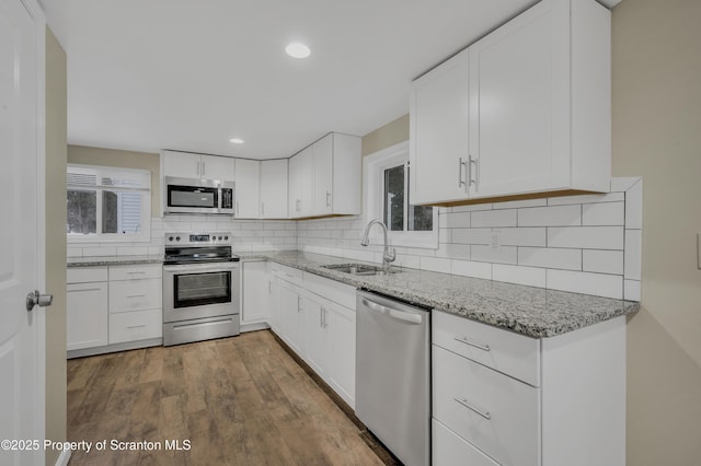 kitchen featuring light stone countertops, white cabinets, wood-type flooring, stainless steel appliances, and sink