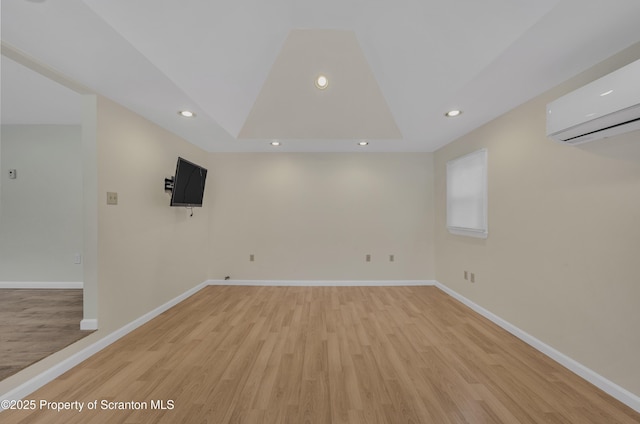 unfurnished room with light wood-type flooring, a raised ceiling, and a wall mounted air conditioner