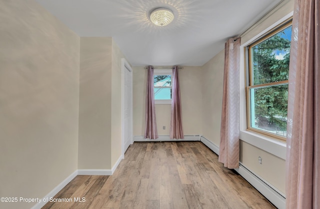 spare room with light wood-type flooring, a healthy amount of sunlight, and a baseboard radiator