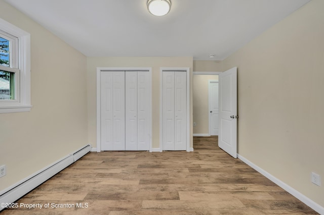 unfurnished bedroom featuring light wood-type flooring, baseboard heating, and multiple closets