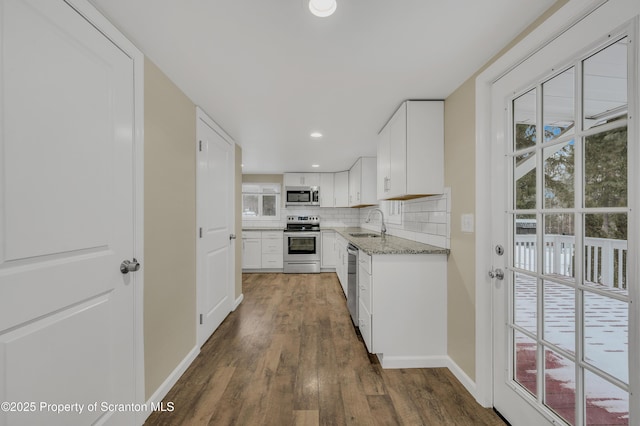 kitchen with sink, dark wood-type flooring, light stone countertops, stainless steel appliances, and white cabinets