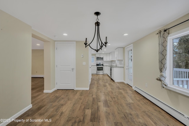 kitchen with decorative light fixtures, backsplash, appliances with stainless steel finishes, white cabinets, and baseboard heating