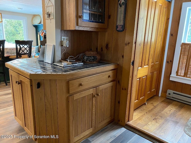 kitchen featuring tile countertops, light wood-style flooring, a baseboard heating unit, and brown cabinetry