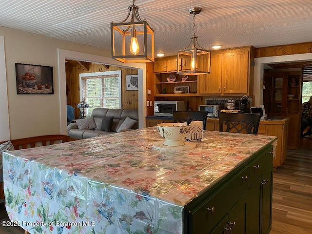 kitchen featuring hanging light fixtures, stainless steel microwave, dark wood-type flooring, and a center island