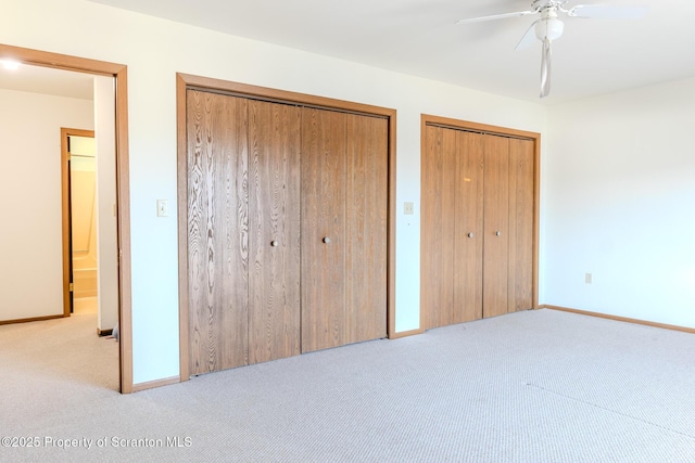 unfurnished bedroom with ceiling fan, light colored carpet, and two closets