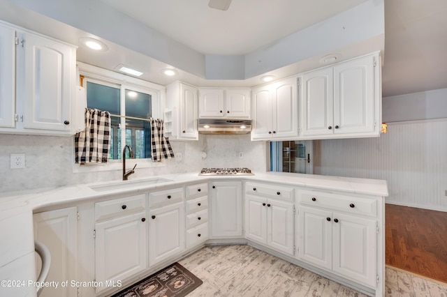 kitchen featuring kitchen peninsula, light stone countertops, sink, white cabinetry, and stainless steel gas stovetop