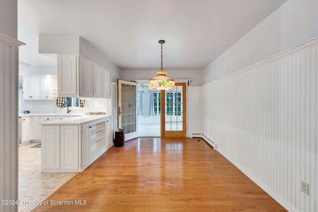 interior space with hanging light fixtures, baseboard heating, light hardwood / wood-style flooring, backsplash, and white cabinets