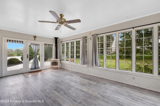 unfurnished sunroom featuring a wood stove and ceiling fan