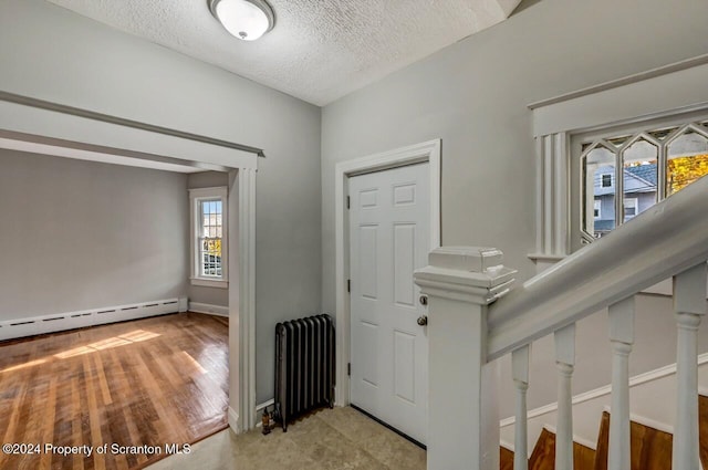 carpeted foyer featuring a baseboard radiator, radiator heating unit, and a textured ceiling