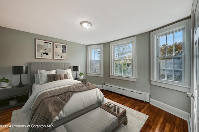 bedroom with dark hardwood / wood-style floors and a baseboard heating unit