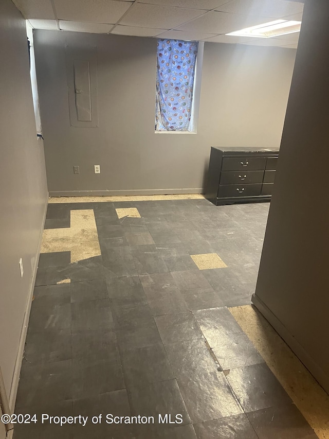 basement featuring a paneled ceiling and electric panel