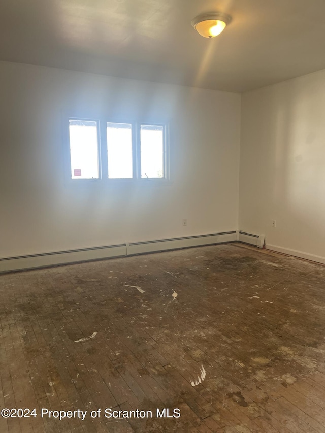 spare room featuring baseboard heating and dark hardwood / wood-style floors