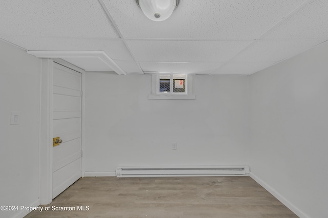 basement with a baseboard radiator, light hardwood / wood-style flooring, and a drop ceiling